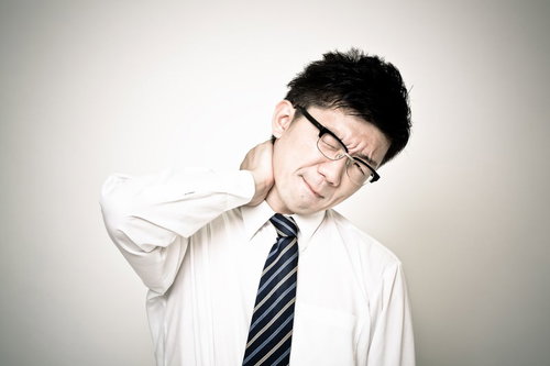 首に手を当てて痛そうな表情の眼鏡のサラリーマン