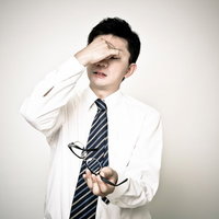 額を押さえ眼鏡を持つ目の奥が痛い表情のサラリーマンの写真