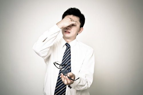 額を押さえ眼鏡を持つ目の奥が痛い表情のサラリーマン