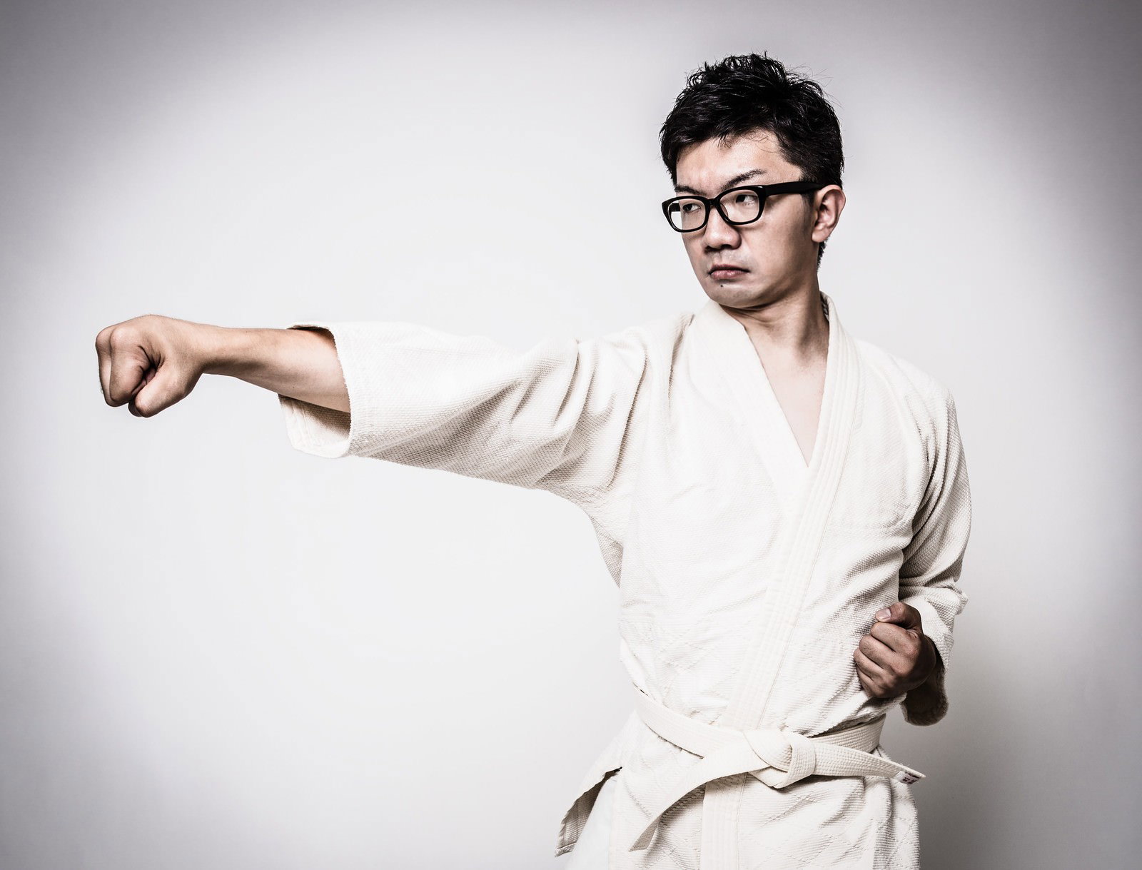 白い道着で正拳突きの構えをとる眼鏡の男性［モデル：OZPA］