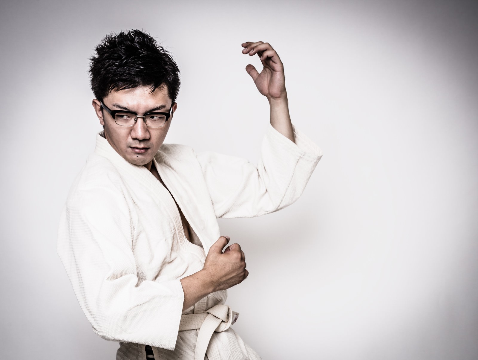 白い道着で右手を上げ左手を腰に当てた構えの眼鏡の男性［モデル：OZPA］