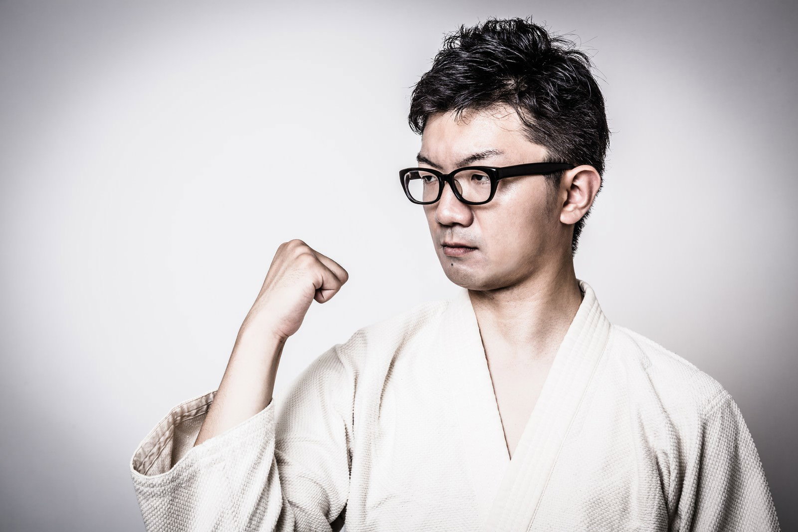 白い道着で右腕を曲げて拳を作る眼鏡の男性［モデル：OZPA］