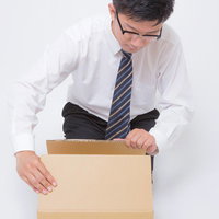 届いたダンボールを開封するサラリーマンの写真
