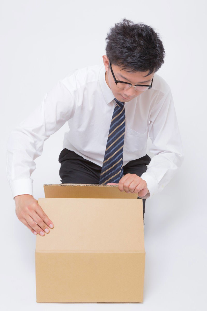 届いたダンボール箱を開封するサラリーマン［モデル：OZPA］