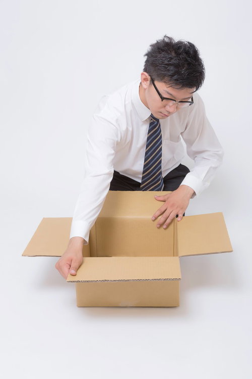 ダンボール箱を丁寧に開ける眼鏡のビジネスマン