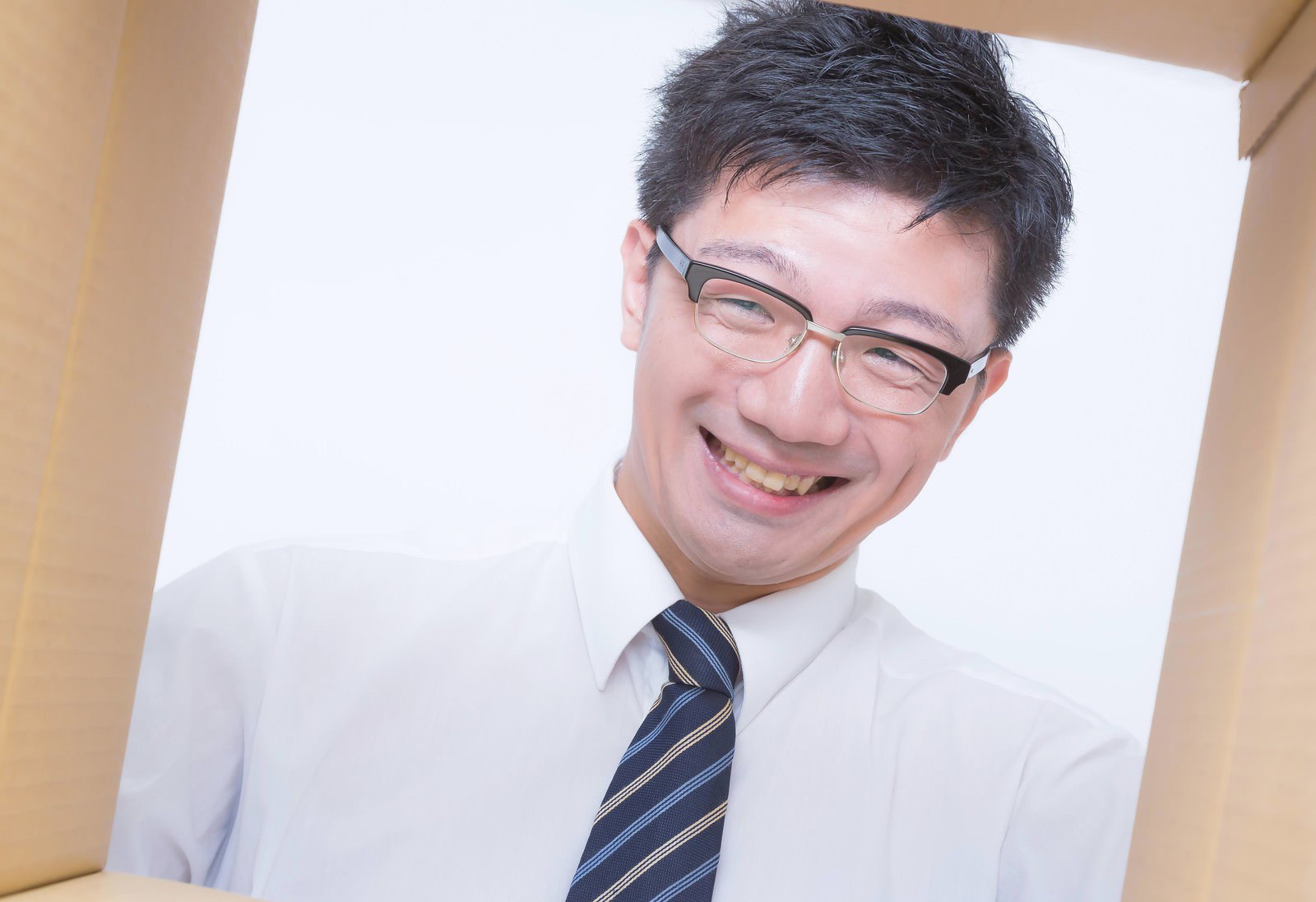 ダンボールに囲まれニンマリ笑う眼鏡のサラリーマン［モデル：OZPA］