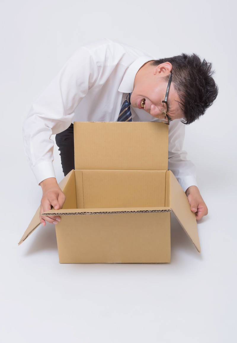 開いたダンボール箱を上から覗き込んで困惑する眼鏡の男性［モデル：OZPA］