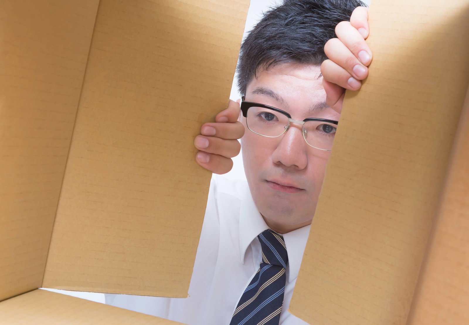 段ボール箱の隙間から顔を出す眼鏡の男性［モデル：OZPA］