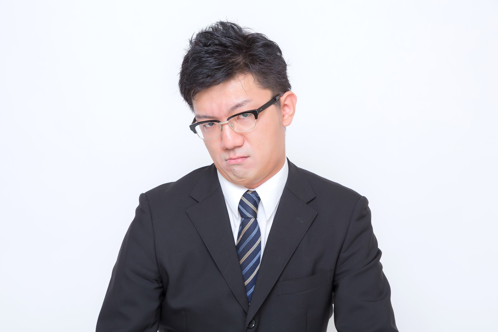 おこな表情で正面を向くスーツ姿の眼鏡の男性［モデル：OZPA］
