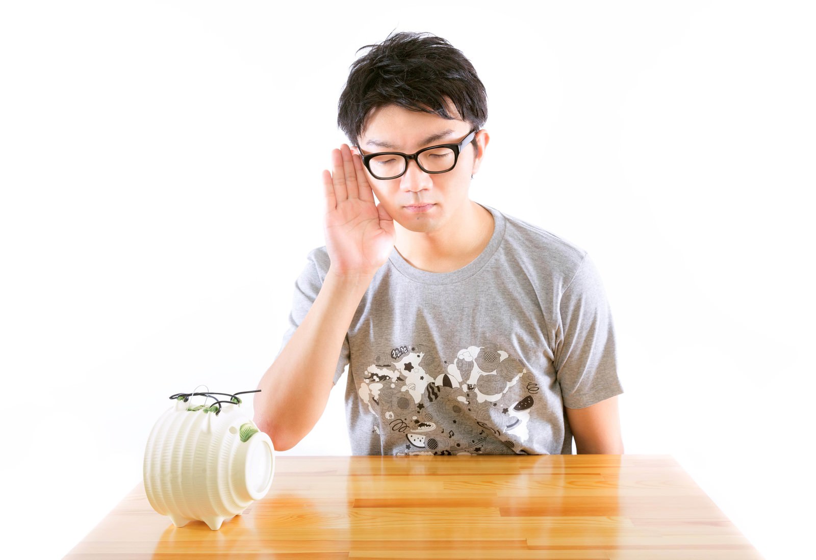 耳に手を当てて机に座る眼鏡の男性［モデル：OZPA］