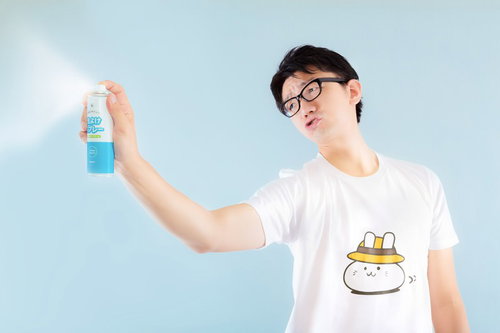 青いスプレー缶を右手で持ち上げる眼鏡の白Tシャツ男性