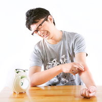 白い豚の貯金箱にコインを入れようとする眼鏡の男性の写真