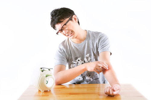 白い豚の貯金箱にコインを入れようとする眼鏡の男性