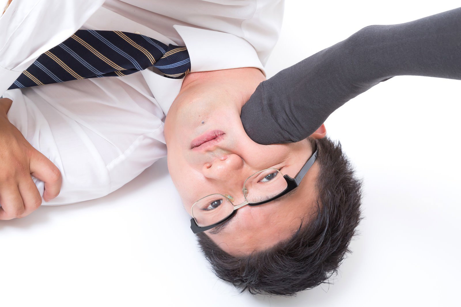 白い床にぐったり横たわるスーツの眼鏡の男性［モデル：OZPA］