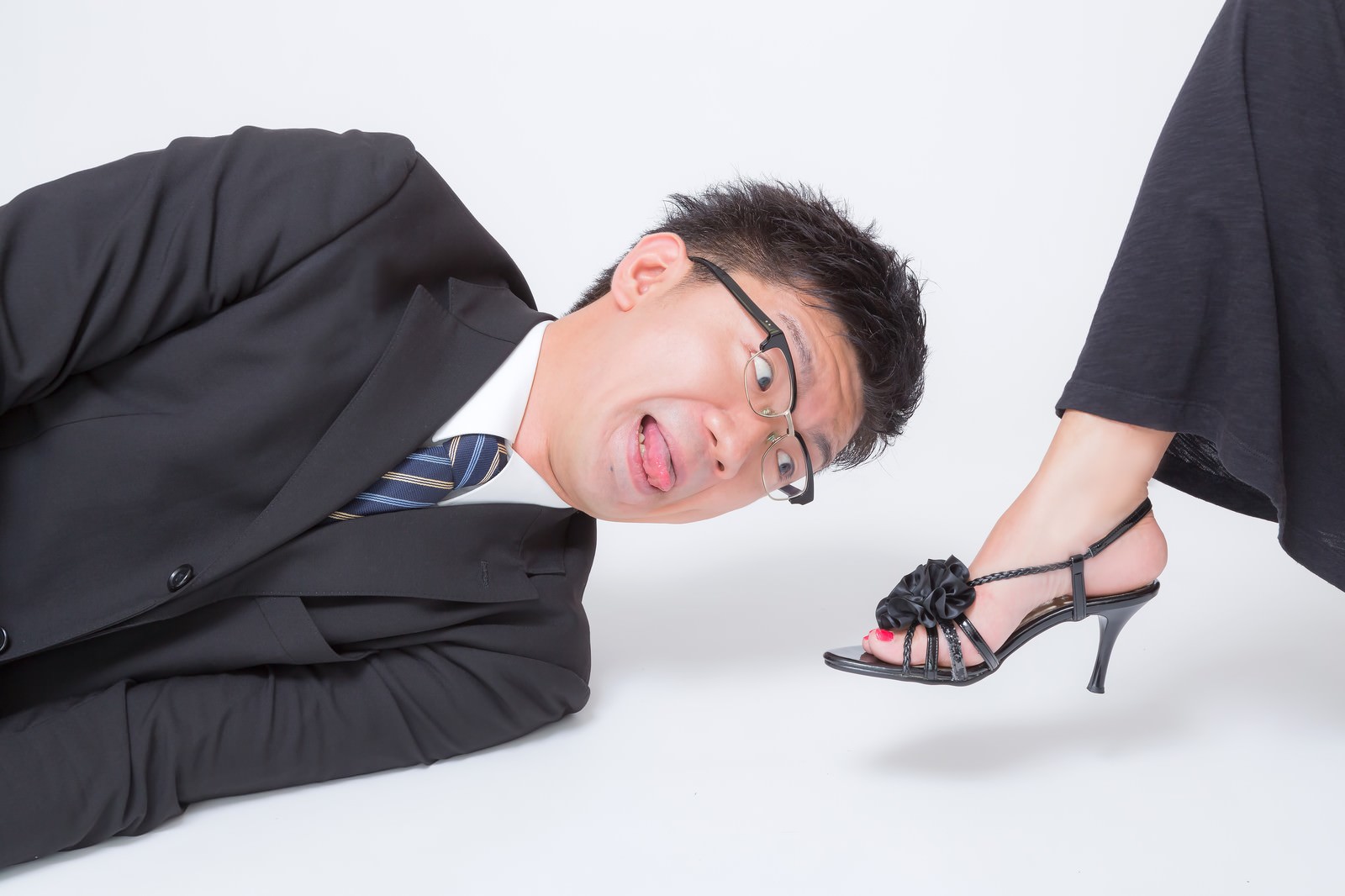 ハイヒールの横で白い床に寝そべるスーツの男性［モデル：OZPA］