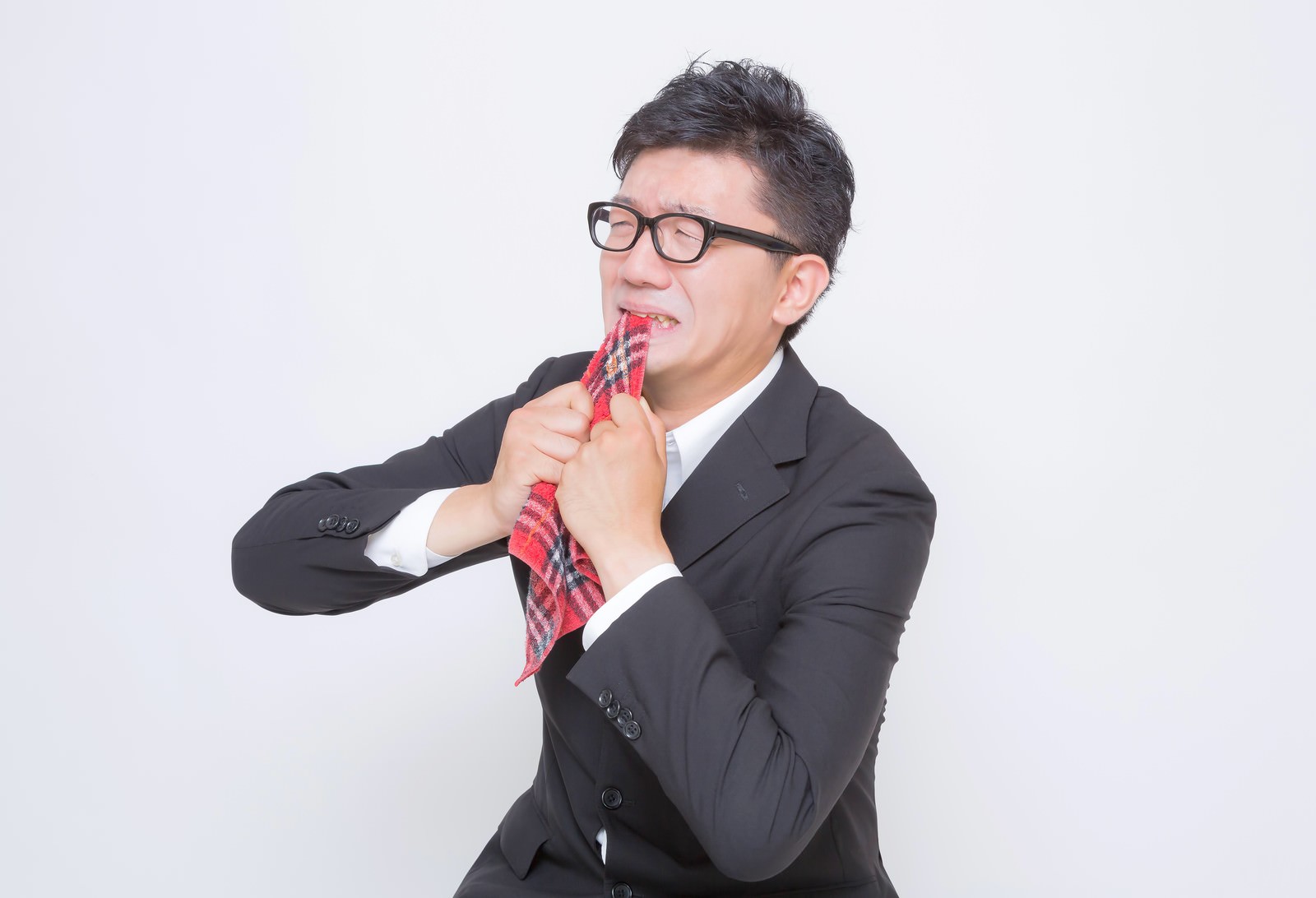 チェック柄のネクタイを噛んで悔しがる眼鏡のサラリーマン［モデル：OZPA］