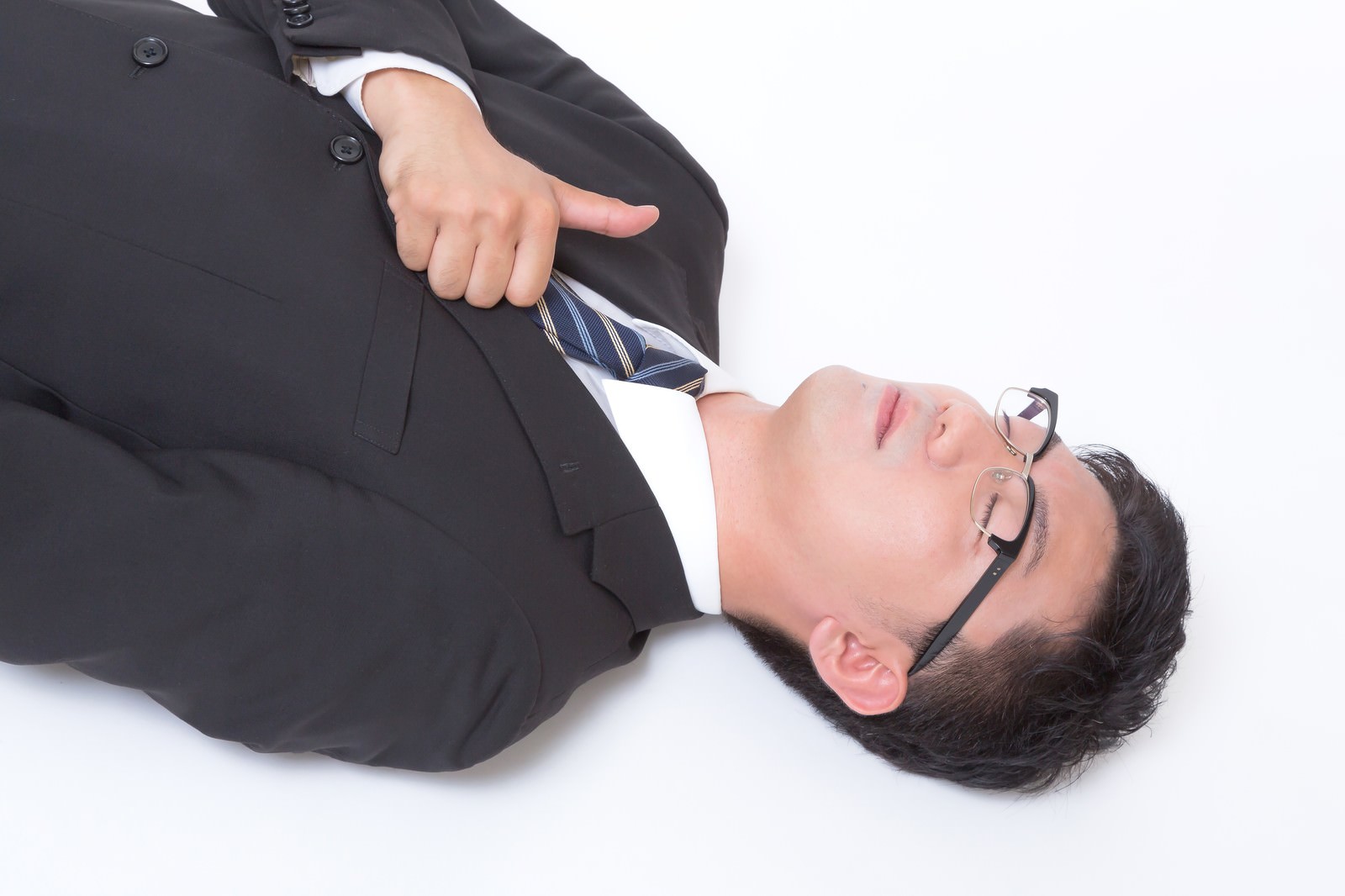 床に横たわりながら親指を立てるスーツの眼鏡の男性［モデル：OZPA］
