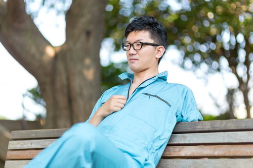 公園のベンチに座る水色ジャケットの男性
