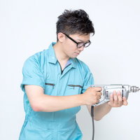 電動ドリルを構える水色の作業服の男性の写真