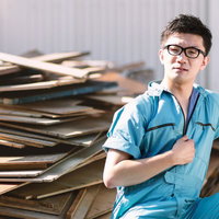 廃材置き場で腕を組む作業服の男性の写真