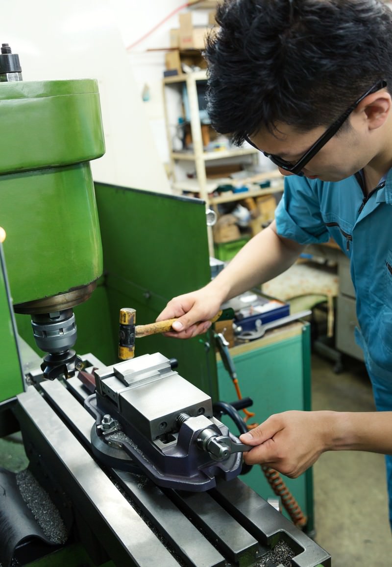 町工場のフライス盤で万力を締める水色作業着の男性作業員［モデル：OZPA］