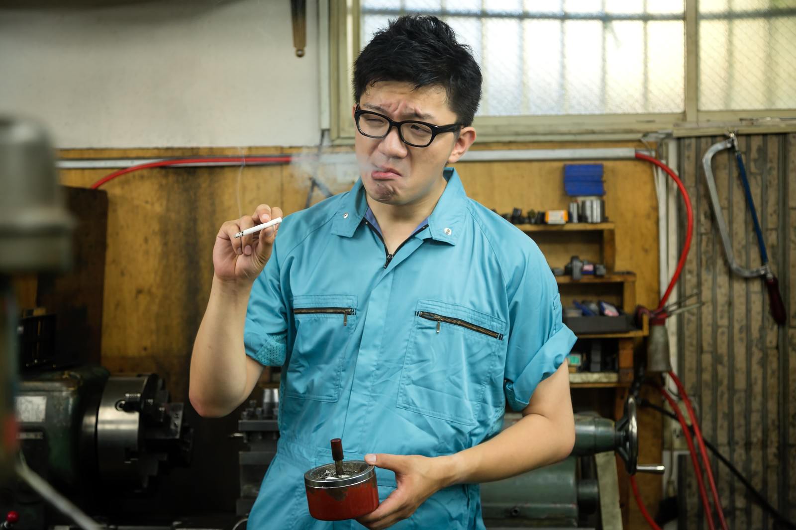 工場内でタバコを吸う作業着姿の男性［モデル：OZPA］