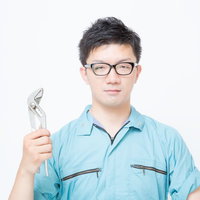 レンチを手にする水色の作業服の男性の写真