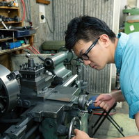 汎用旋盤で中グリ用刃物の芯高を確認し、ハンドルで調整中の男性の写真