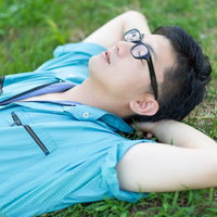 芝生に寝転んで空を眺める作業服の男性の写真