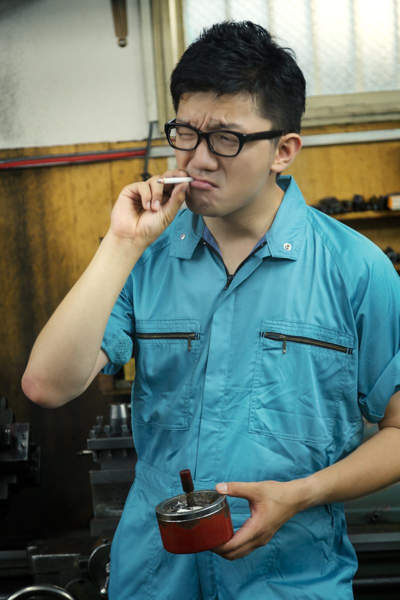 工場で煙草を吸う作業着姿の男性［モデル：OZPA］