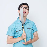 ノコギリを顔の前に立てる作業服の男性の写真