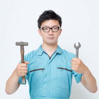ハンマーとスパナを両手に持つ作業服の男性の写真