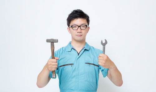 ハンマーとスパナを両手に持つ作業服の男性