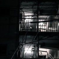 深夜に照らされるマンションの古い非常階段と雑草の写真