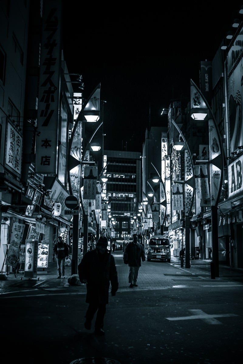 夜間の上野駅前商店街で人が歩く光景。ネオンと街灯で照らされた繁華街