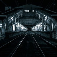 深夜の駅ホームと真っすぐに伸びる線路、照明と電線の写真