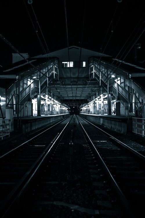 深夜の駅ホームと真っすぐに伸びる線路、照明と電線の写真