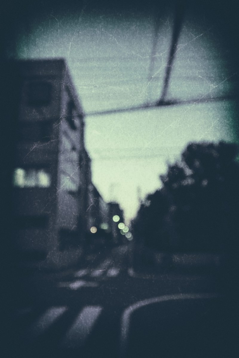 ノイズ感のある古い写真風の夕暮れ時の街並み。街灯の光が暗い建物のシルエットを照らす