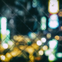 フェンスごしに見たボケた繁華街の夜景の写真