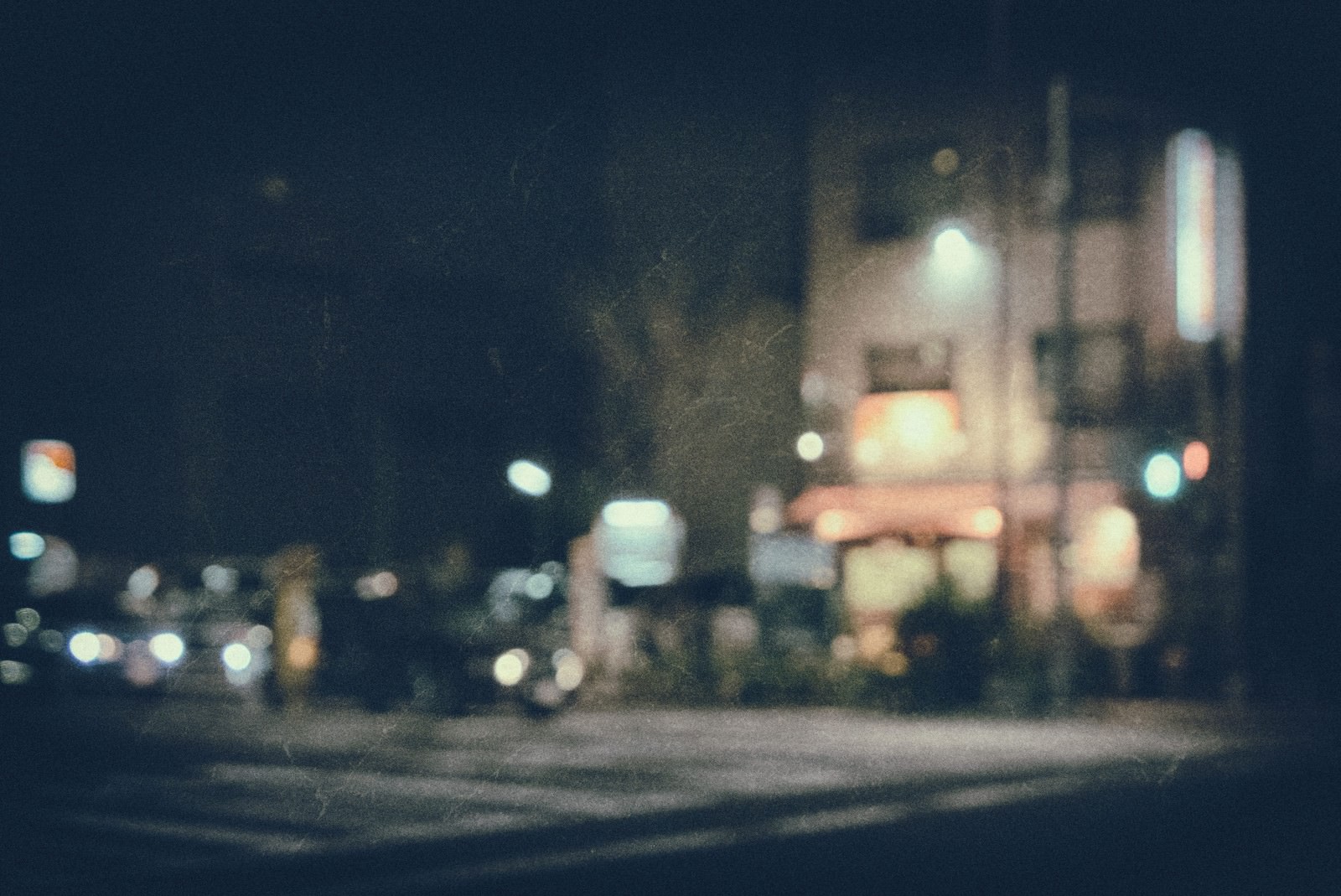 ノイズが入った郊外の飲み屋の夜間風景。街灯と看板の光がぼやけている