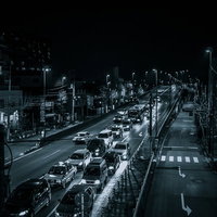 夜間の幹線道路で信号待ちする車列と街灯に照らされた都市景観の写真
