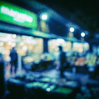 夜間営業のスーパーの店頭、光のボケと街灯の夜景の写真