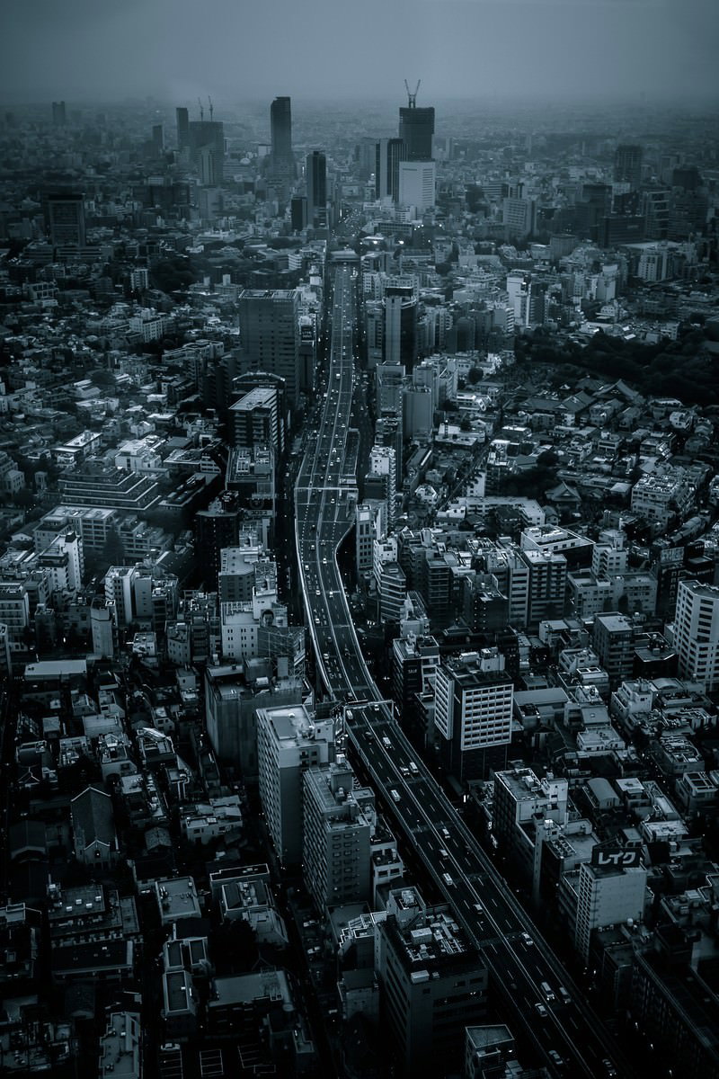 雨の日の都会を俯瞰した写真。ビル群と住宅街の中央を幹線道路が走る
