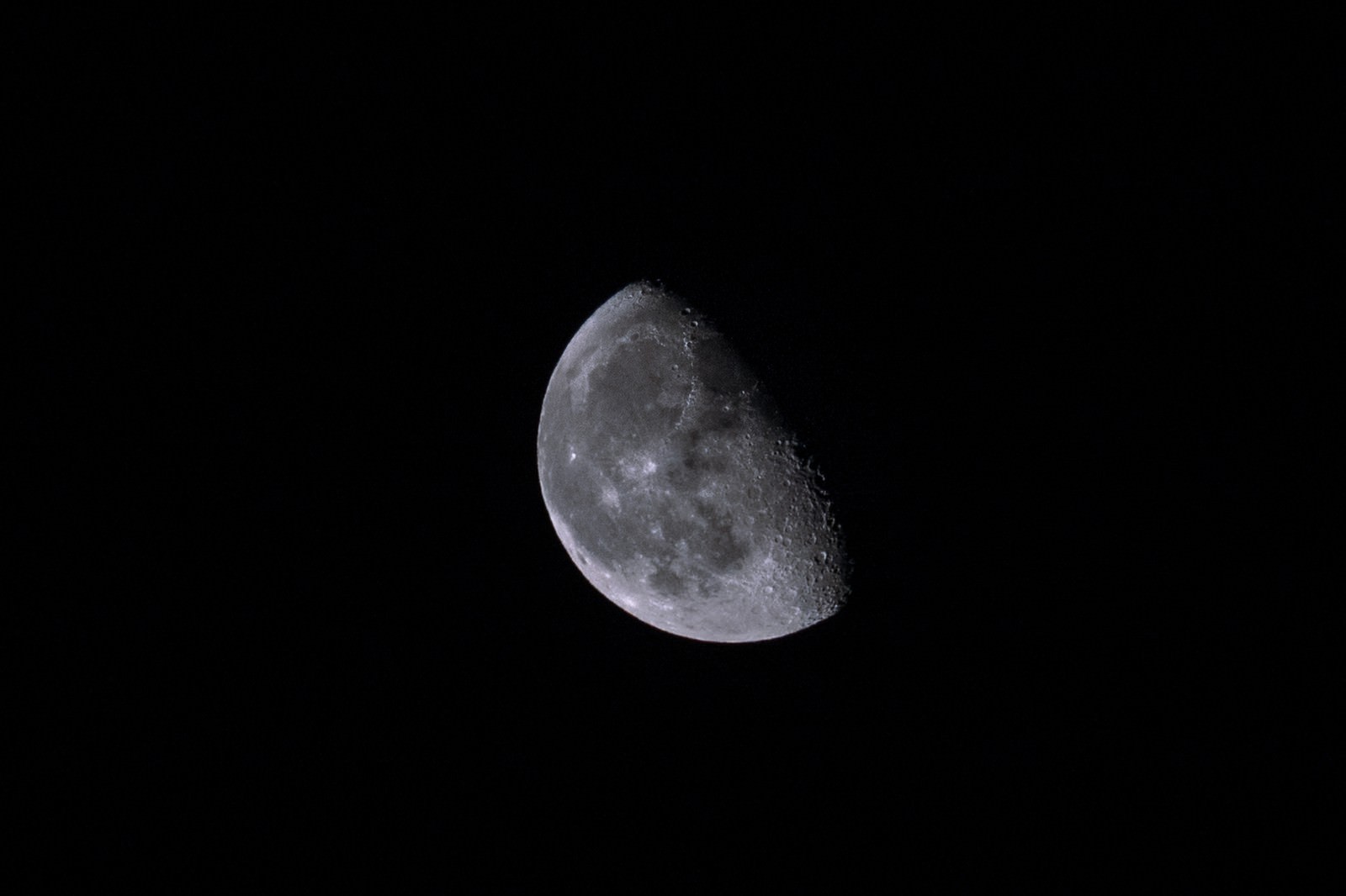 黒い夜空に浮かぶ半月。左側は明るく光り、右側の陰となった部分がクレーターと共に見える