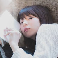 ソファーに寝転がりマンガを読む美女のリラックスショットの写真