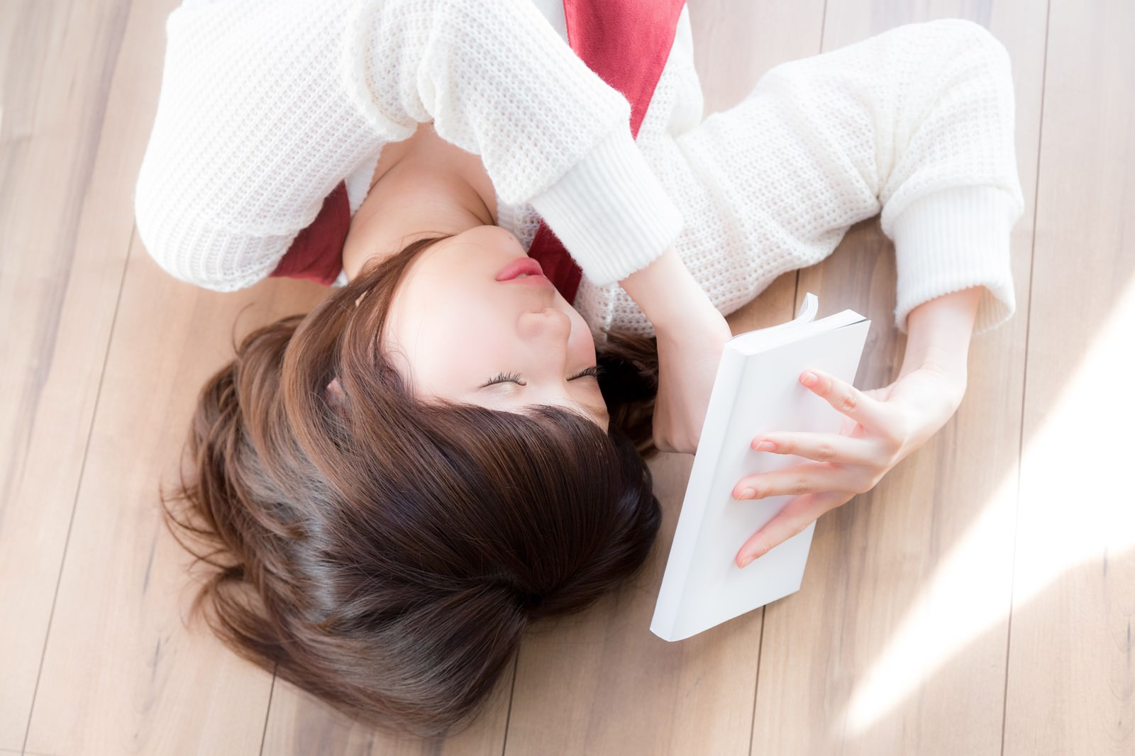 白いセーター姿でマンガ本を持ったまま床で寝ている女性［モデル：みき。］