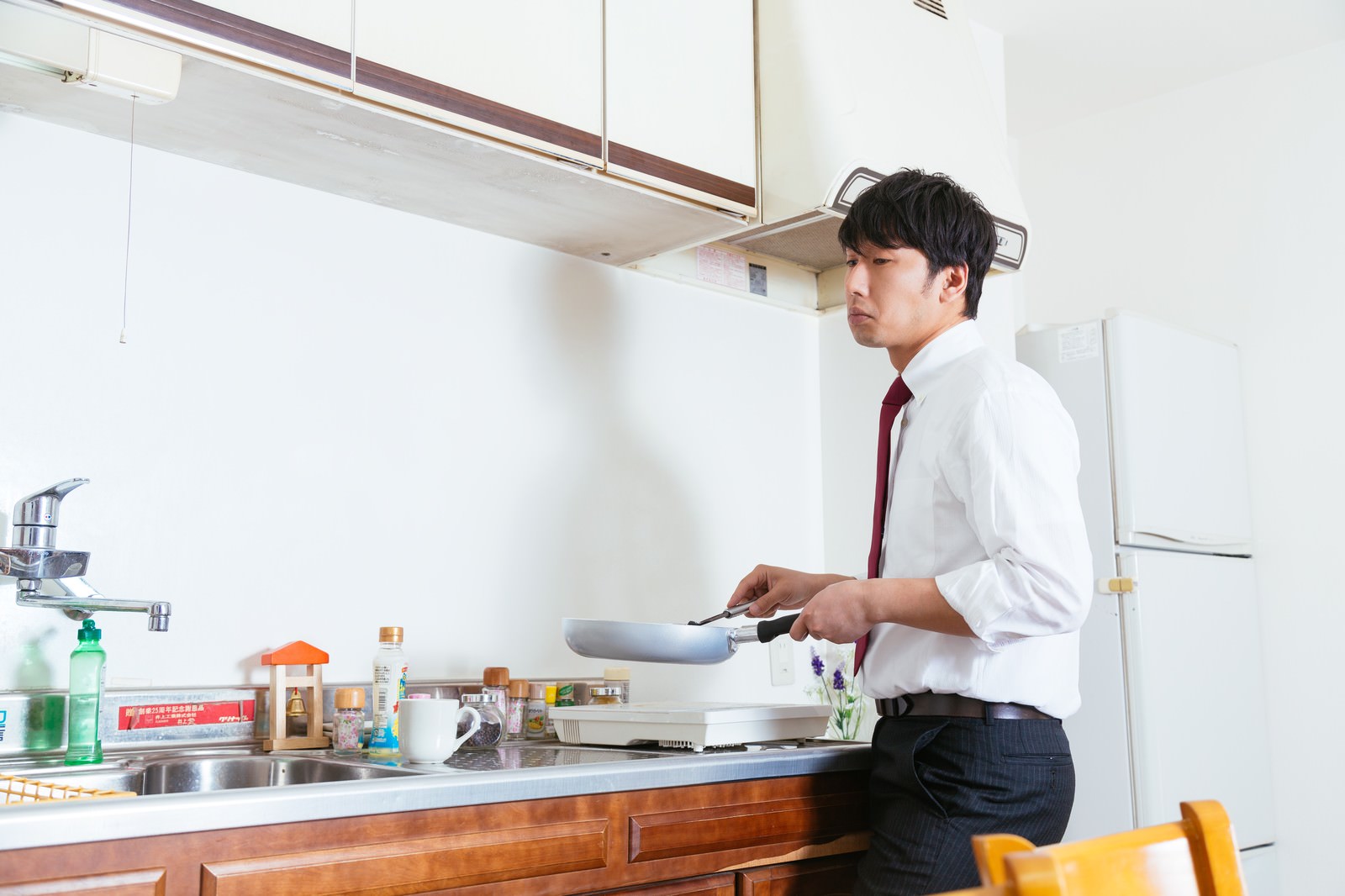 キッチンで虫を見つけ、フライパンを持ちながら考える男性［モデル：大川竜弥］