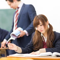 教室で教科書を広げて真面目に授業を受ける女子高生と崩壊気味の男子高生の写真