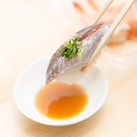 箸でつまんだアジの握り寿司と醤油の写真
