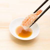 黒い箸でエビの握り寿司を醤油につけるの写真